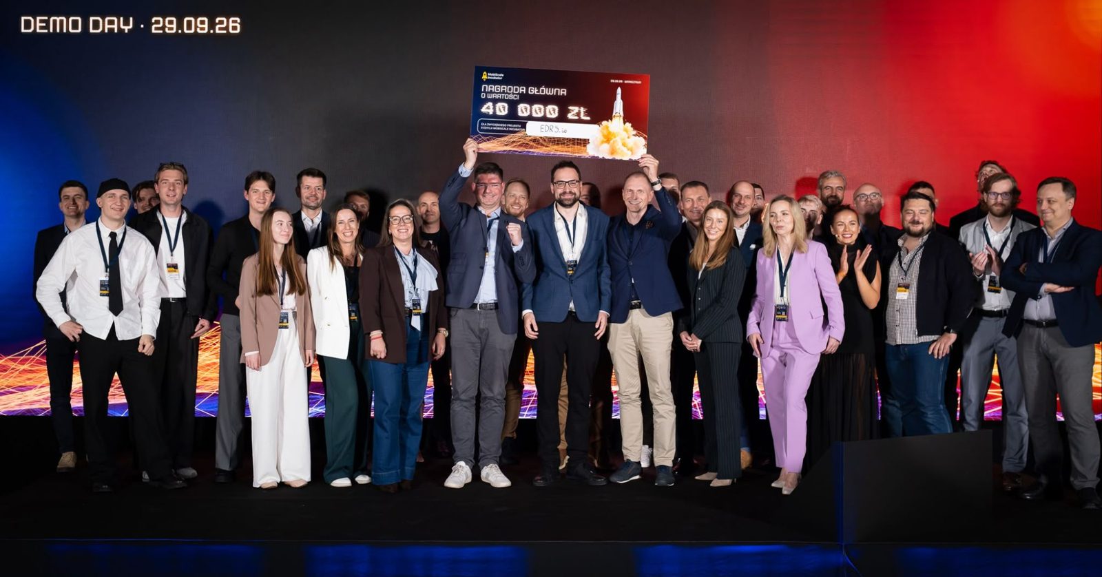 Finaliści, mentorzy i organizatorzy na scenie Demo Day MobiScale, czek dla EDRS.io w górze